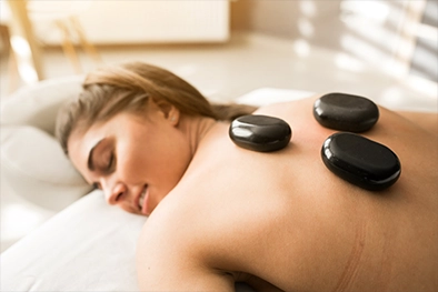Warm massage oil being poured into therapist’s hand near treatment table