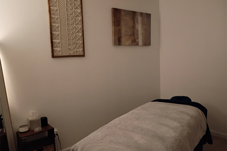 Brenda standing in treatment room beside massage table and soft wall lighting